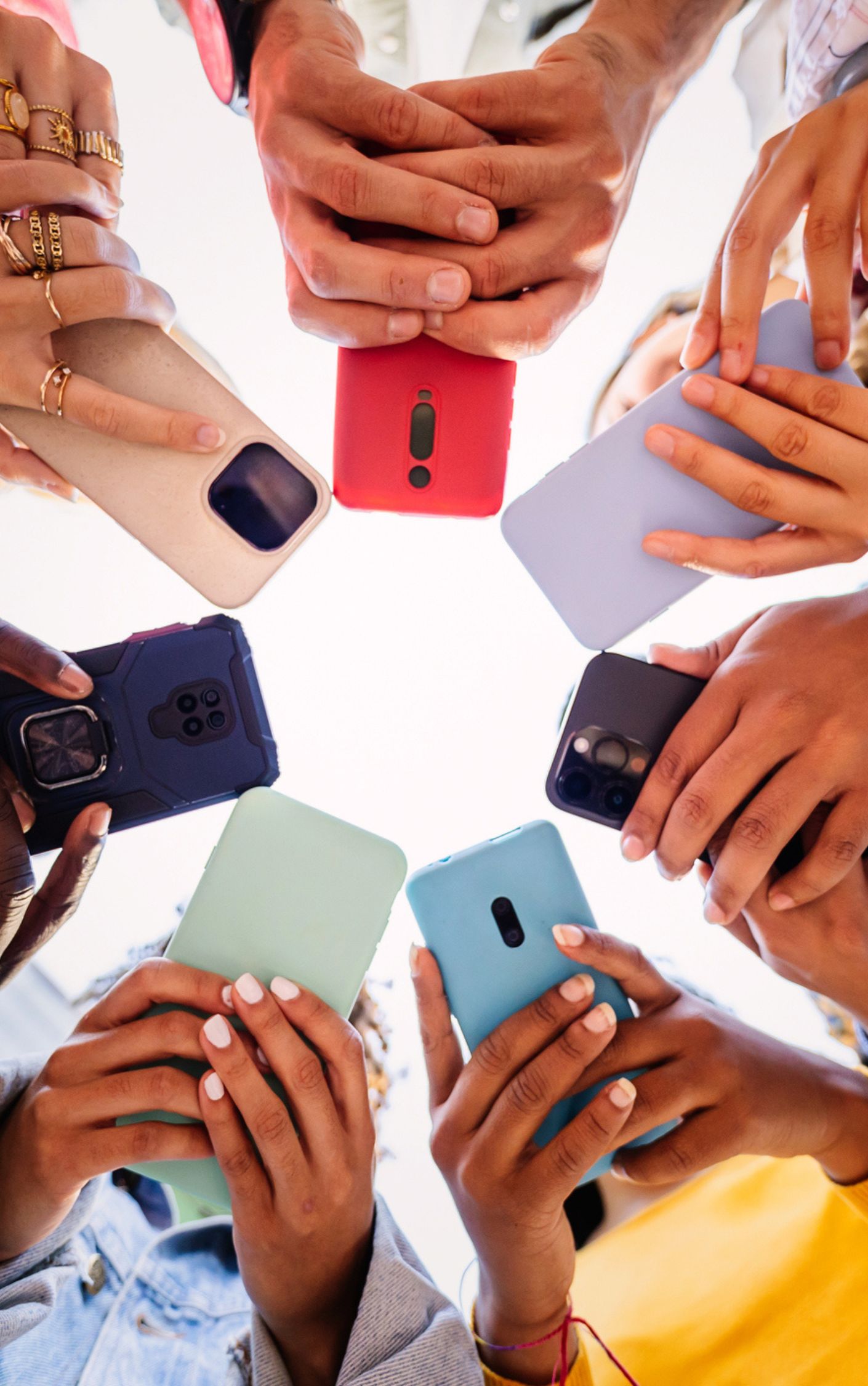 Diverse group of people holding smartphones in a circle, viewed from below, symbolizing digital connection, youth engagement, and social media culture.